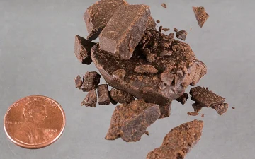 Broken pieces of hashish beside a coin for scale