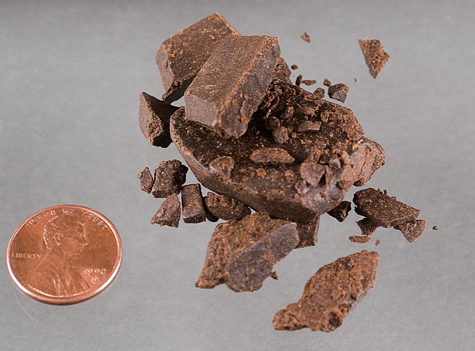 Broken pieces of hashish beside a coin for scale