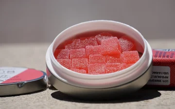A tin of pink cannabis gummies beside its packaging