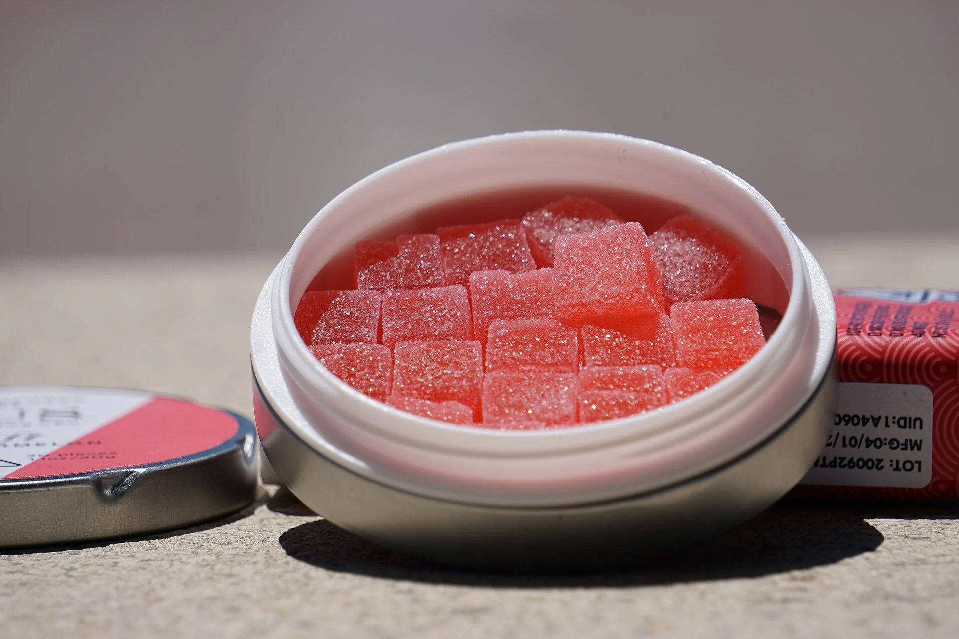 A tin of pink cannabis gummies beside its packaging