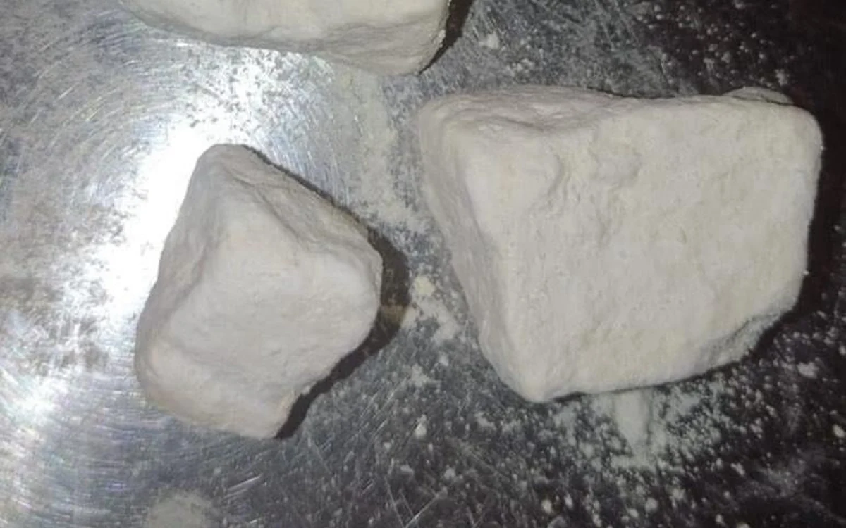 Two white chunks of amphetamine on a metal surface with loose white powder