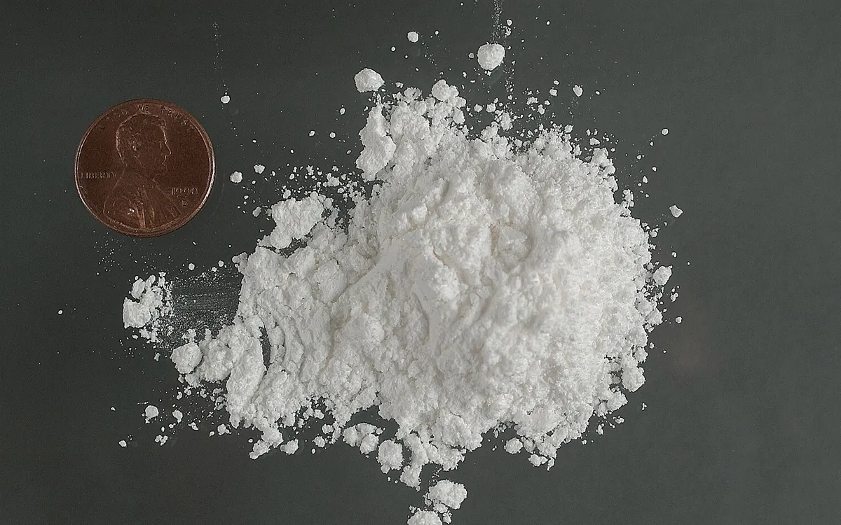 A heap of white cocaine hydrochloride powder beside a one cent coin for scale
