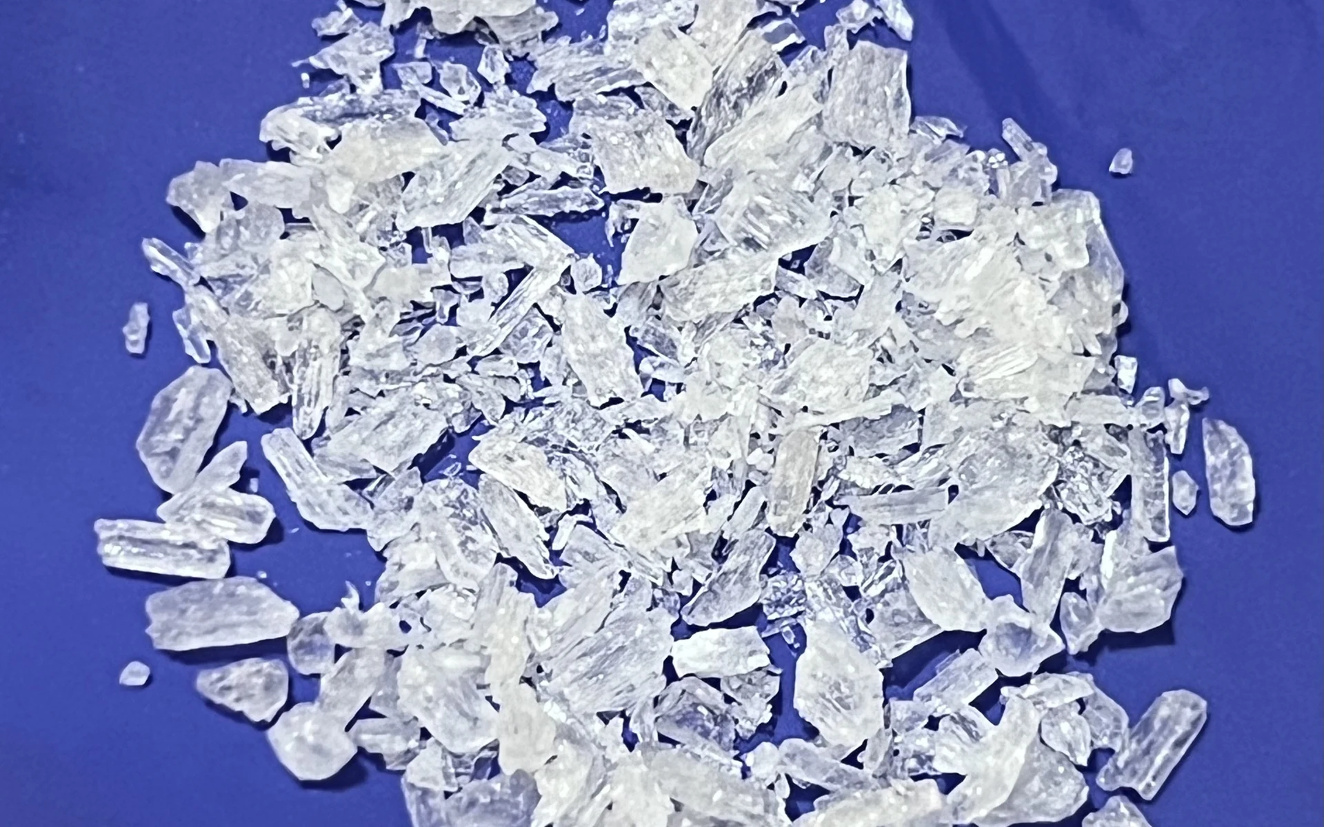A heap of clear methamphetamine crystal shards of mixed size on a deep blue cloth background