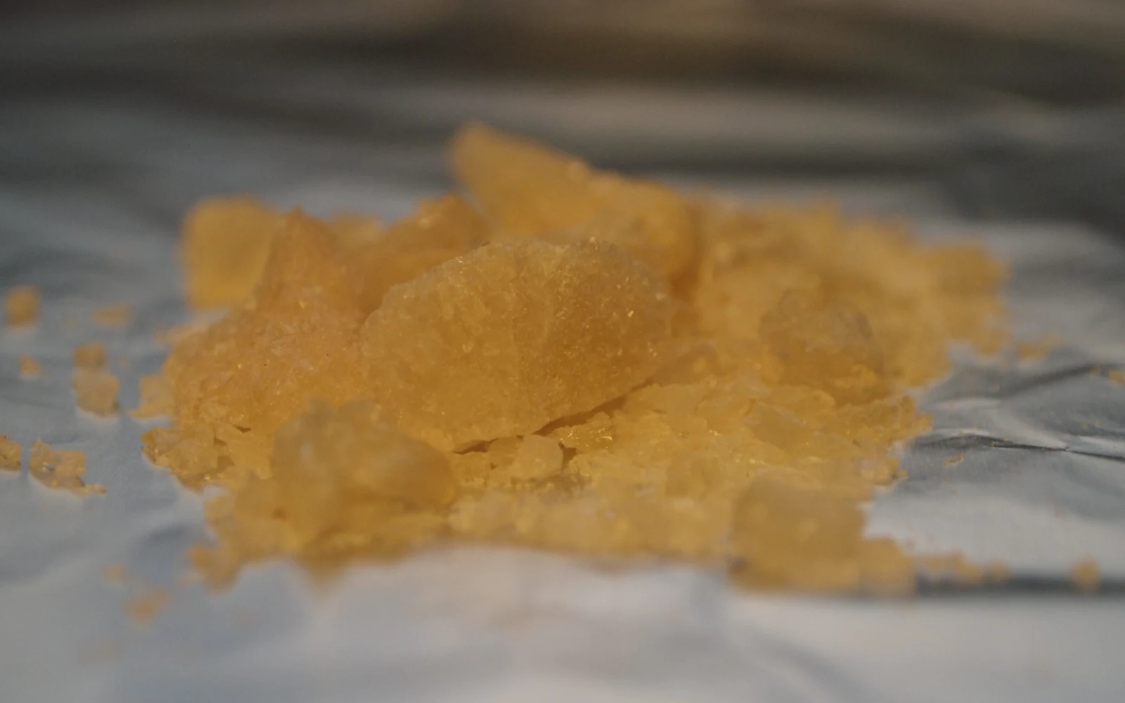 Amber and tan MDMA crystal shards photographed on grey paper