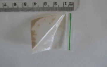 Small bag holding brown heroin residue, photographed beside a ruler